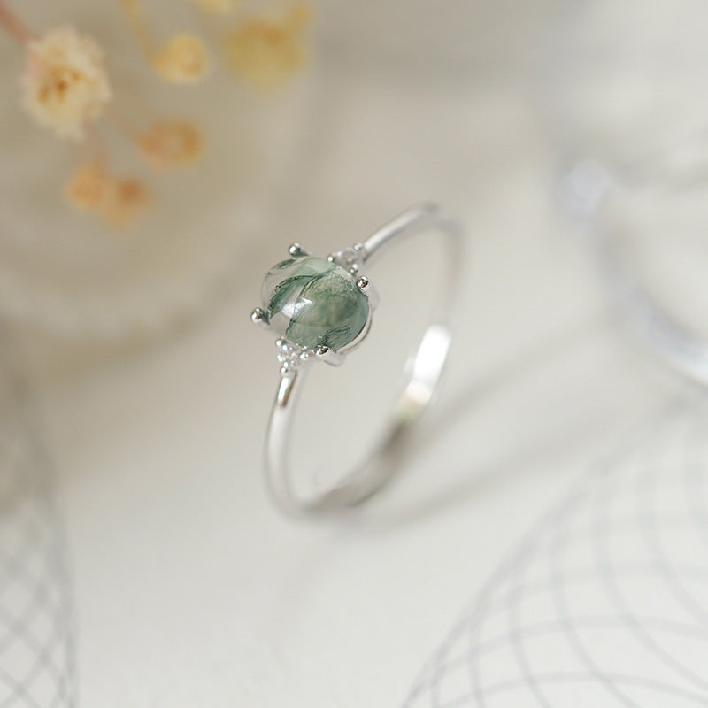 An S925 silver ring with a green moss agate centerpiece, presented on a white background with floral accents.